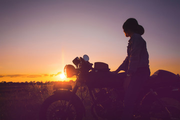 Silhouette of young woman drive with motorcycle on street, enjoying freedom and active lifestyle, having fun on a bikers tour on sunset background. © EsanIndyStudios