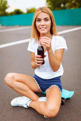 Girl with a skate in the Park, drinking a drink with a glass bottle