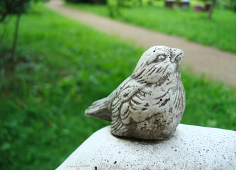 Stone sculpture little sparrow in the Park on a green background.