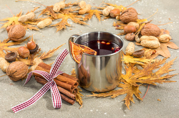 Mulled wine in metal rustic mug with spices and citrus fruits decorated with autumn leaves and...