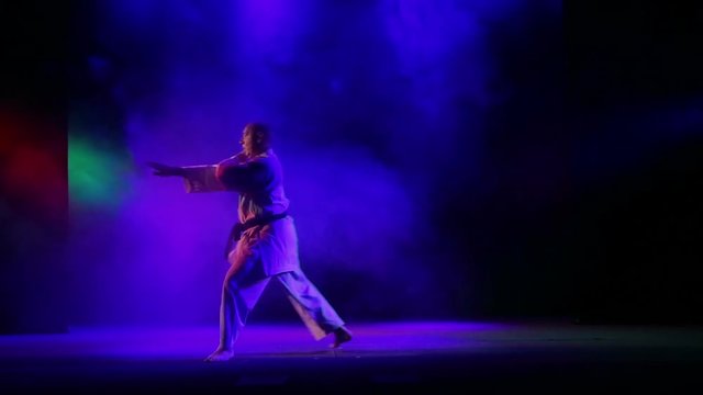 A man in a kimono with a black belt performs karate exercises on a black background with colored smoke