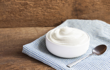 Healthy flavored yogurt in ceramic bowl and spoon on cloth with wood background with copy space for your text.