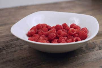 Bowl of red raspberries on a wood table
