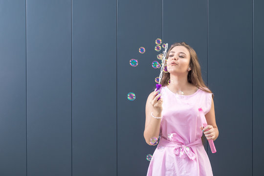 Teenage girl in beautiful dress blowing soap bubbles