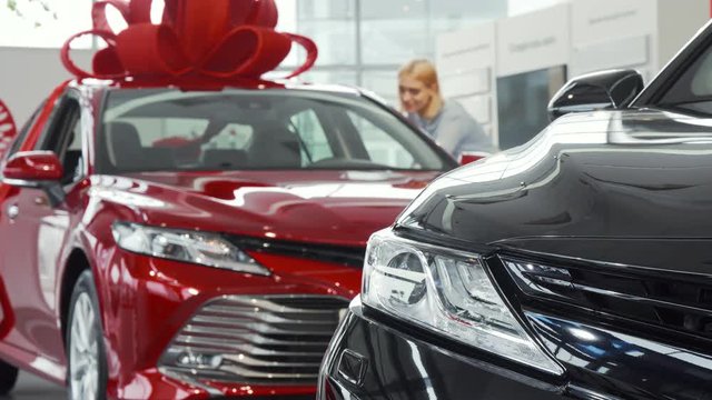 Selective focus on a car light, copy space. Young cheerful woman smiling while choosing a new car at the dealership showroom. Female customer examining automobile for sale.