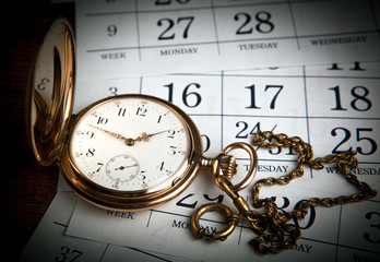 An antique gold pocket watch lies on calendar sheets
