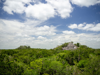 Fototapeta na wymiar Two ancient Mayan stone structures rising out of the jungle canopy at Calakmul, Mexico