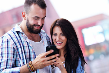 Happy couple using smartphone in city in rainy day