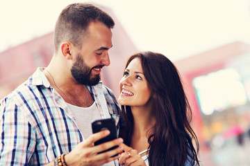 Happy couple using smartphone in city in rainy day