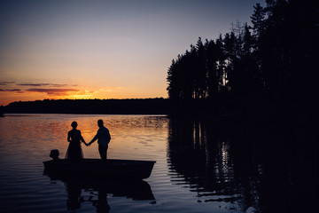 Naklejka na ściany i meble Silhouette of two lovers in boat on the lake at sunset. Photosession of couple on water