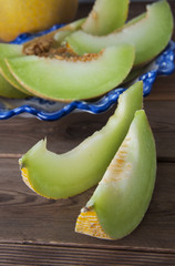 Cantaloupe yellow fresh melon slices isolated with beautiful vintage blue plate on background, wooden table background. Summer fruits.