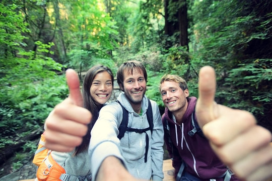 Hiking group of friends travel lifestyle young people happy doing thumbs up at selfie photo . Three young men and woman having fun backpacking in nature camping.