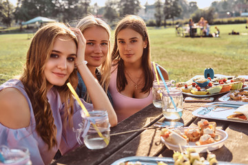 Group of happy girlfriends sitting at the table together celebrating a birthday at the outdoor park.