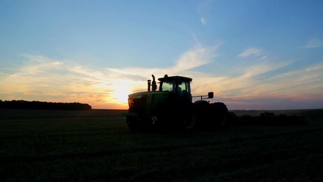 The tractor plows a field at sunset. Agricultural field treatment by tractor at sunset of the day.
