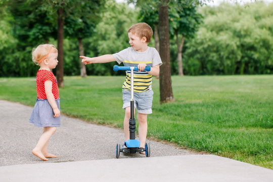 Two Little Caucasian Preschool Children Fighting In Park Outside. Boy And Girl Can Not Share One Scooter. Older Sibling Brother Not Giving His Toy To Younger Sister. Communication Problems.