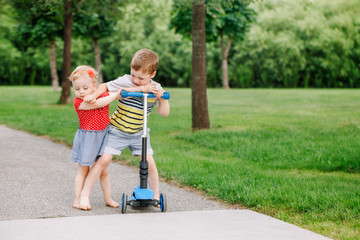 Two little Caucasian preschool children fighting hitting each other. Boy and girl can not share one scooter. Older sibling brother not giving his toy to younger sister. Communication problems. - 217033981