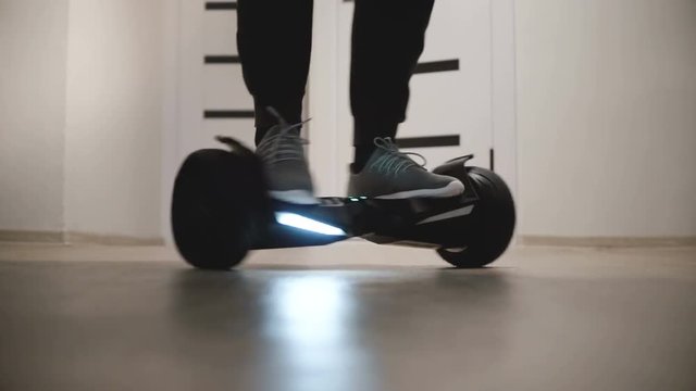 Close-up view of male legs moving around on electric gyro scooter in apartment with white walls, then walking away.