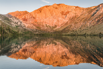 Fototapeta na wymiar Sunrise casts golden light on mountain peaks reflected in the calm waters of Convict Lake in the eastern Sierra Nevada mountains of California