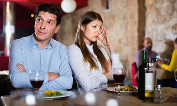Young emotional couple quarreled in restaurant sitting at served table