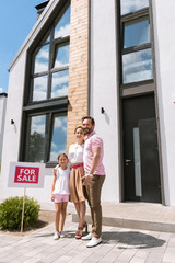 New home. Joyful positive family standing near the house while buying it