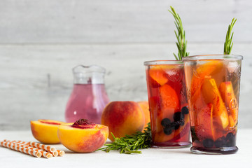 Peach and rosemary lemonade or cocktail in glass with fresh peaches on a light gray background. Summer cold drink.