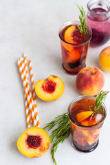 Peach and rosemary lemonade or cocktail in glass with fresh peaches on a light gray background. Summer cold drink.
