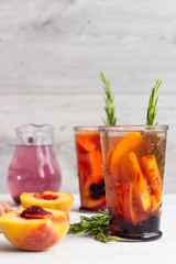 Peach and rosemary lemonade or cocktail in glass with fresh peaches on a light gray background. Summer cold drink.