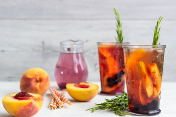 Peach and rosemary lemonade or cocktail in glass with fresh peaches on a light gray background. Summer cold drink.