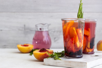 Peach and rosemary lemonade or cocktail in glass with fresh peaches on a light gray background. Summer cold drink.