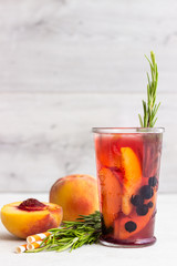 Peach and rosemary lemonade or cocktail in glass with fresh peaches on a light gray background. Summer cold drink.