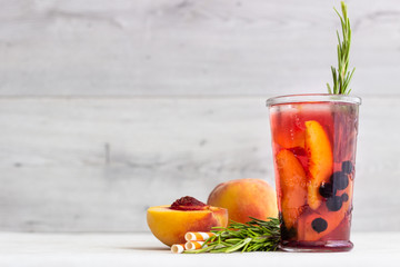 Peach and rosemary lemonade or cocktail in glass with fresh peaches on a light gray background....