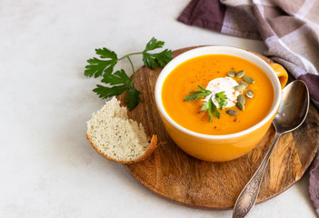 Roasted pumpkin soup with cream, parsley and pumpkin seeds on light background. 