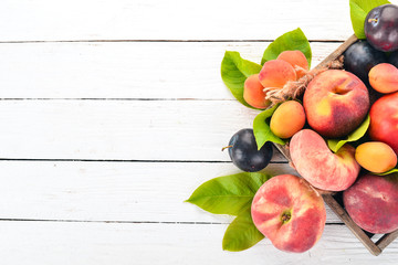 Fresh fruits in a wooden box. Apricot, peach, nectarine, plum. On a wooden background. Top view. Free space for your text.