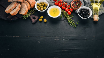 A set of olives, olive oil, bread, cheese and spices. On a black wooden background. Free space for text.