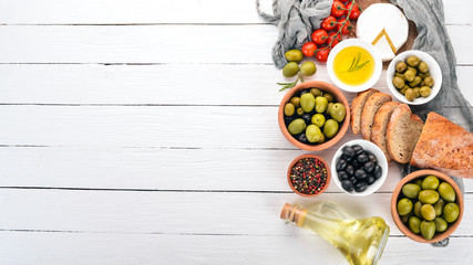 Green olives and black olives, oil, bread, cheese and snacks. Italian cuisine. On a white wooden table. Top view. Free space for text.