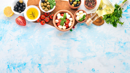 Cooking a caprese salad. Mozzarella cheese, cherry tomatoes, olives, basil leaves. Top view. On a white stone table. Free space for text.