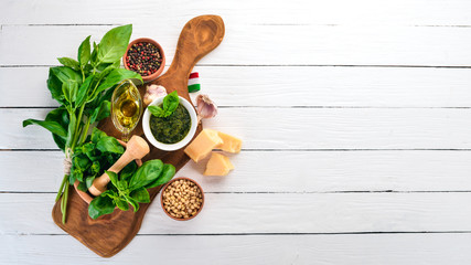 Traditional basil pesto sauce. Basil, parmesan cheese, olive oil. Top view. On a white wooden background. Free space for text.