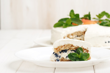 Close up slice of homemade cream cheese cake with fresh fruits and blueberries and mint on white plate on light wood background 