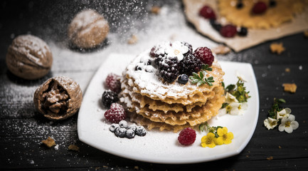 fresh viennese waffles with berries sprinkled with powdered sugar on blackboard on blank background