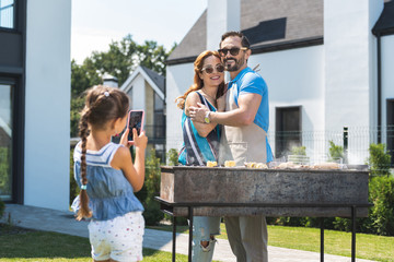 Naklejka premium My parents. Cute nice girl looking at her parents while taking a photo of them