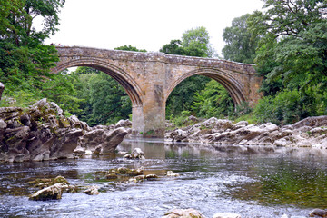Fototapeta na wymiar The Devil’s Bridge Kirkby Lonsdale Cumbria, an historic gritstone bridge over the River Lune.Landscape with a foreground of limestone rocks and river flowing under the bridge
