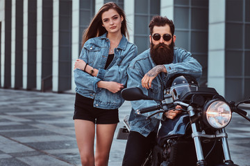 Attractive hipster couple - bearded brutal male in sunglasses and jeans jacket sitting on a retro...
