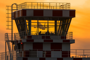 Airplane flying behind airport control tower during sunset. Passnger plane take off view through ATC tower glasses.