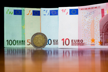 Close Up Euro Money Banknotes And Two Euro Coin. cash Background. Money Bills With Reflection On The Table In Vertical Position. Finance And Economy Concept.