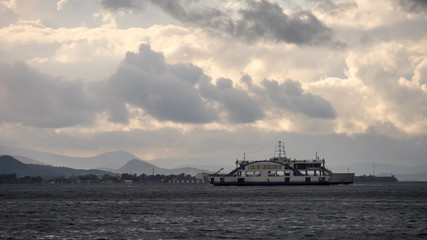 A ferry boat is navigating in the sea in front of the turkish city of Izmir, Turkey, during the fluffy cloudy sky
