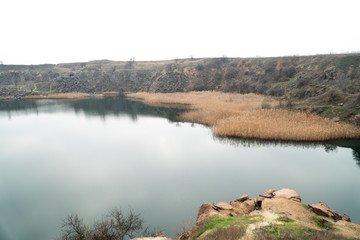 A water-filled quarry with a rocky shore. Sprouted reeds in different places