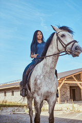 Brunette female riding a dapple gray horse outside.