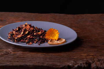 Black dry fruit tea leaves in blue plate on wooden table. Selective focus