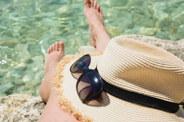 Female accessory, straw sunhat, glasses and long legs. Clean sea. Summer vacation. Close up.