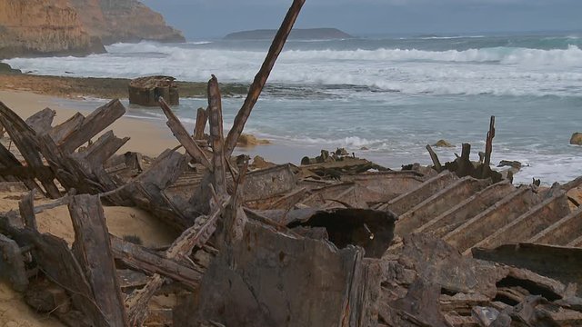 Wide shot of a beach covered in a ship wreck's rust debris with steep cliffs and rough surf in the background